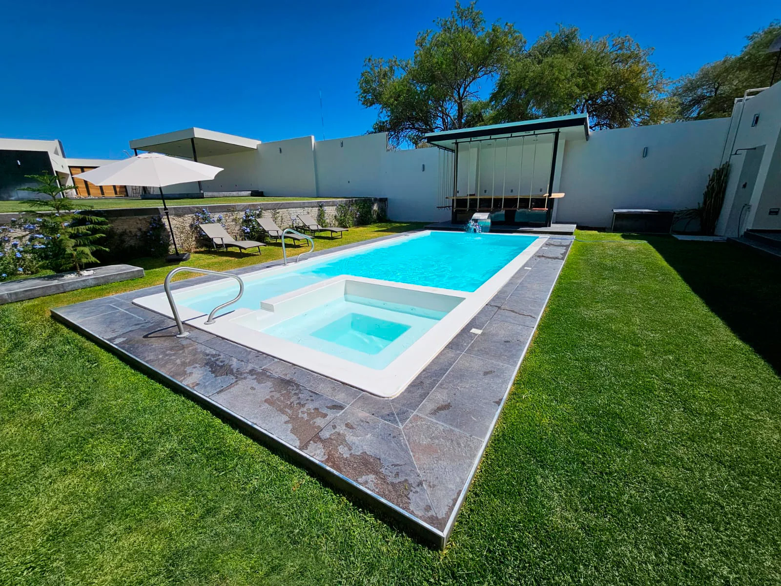 Piscina X-Pools con área de spa integrada en un jardín residencial
